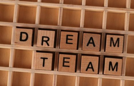 Wooden blocks spelling 'Dream Team' arranged on a wooden grid background.